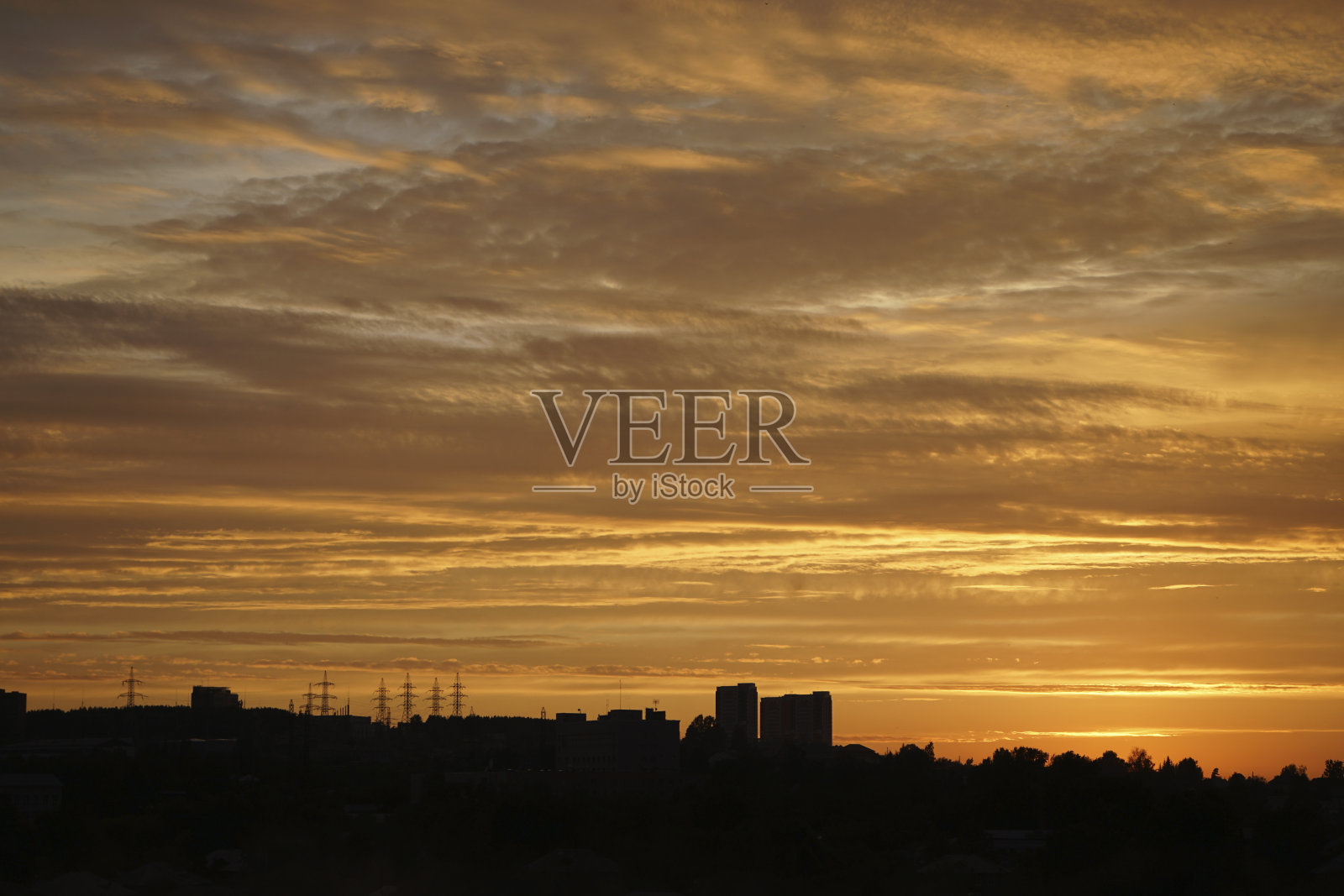 城市上空金色的夕阳。五颜六色的橙黄红色夕阳背景。天空和云朵映衬下的建筑物剪影。照片摄影图片