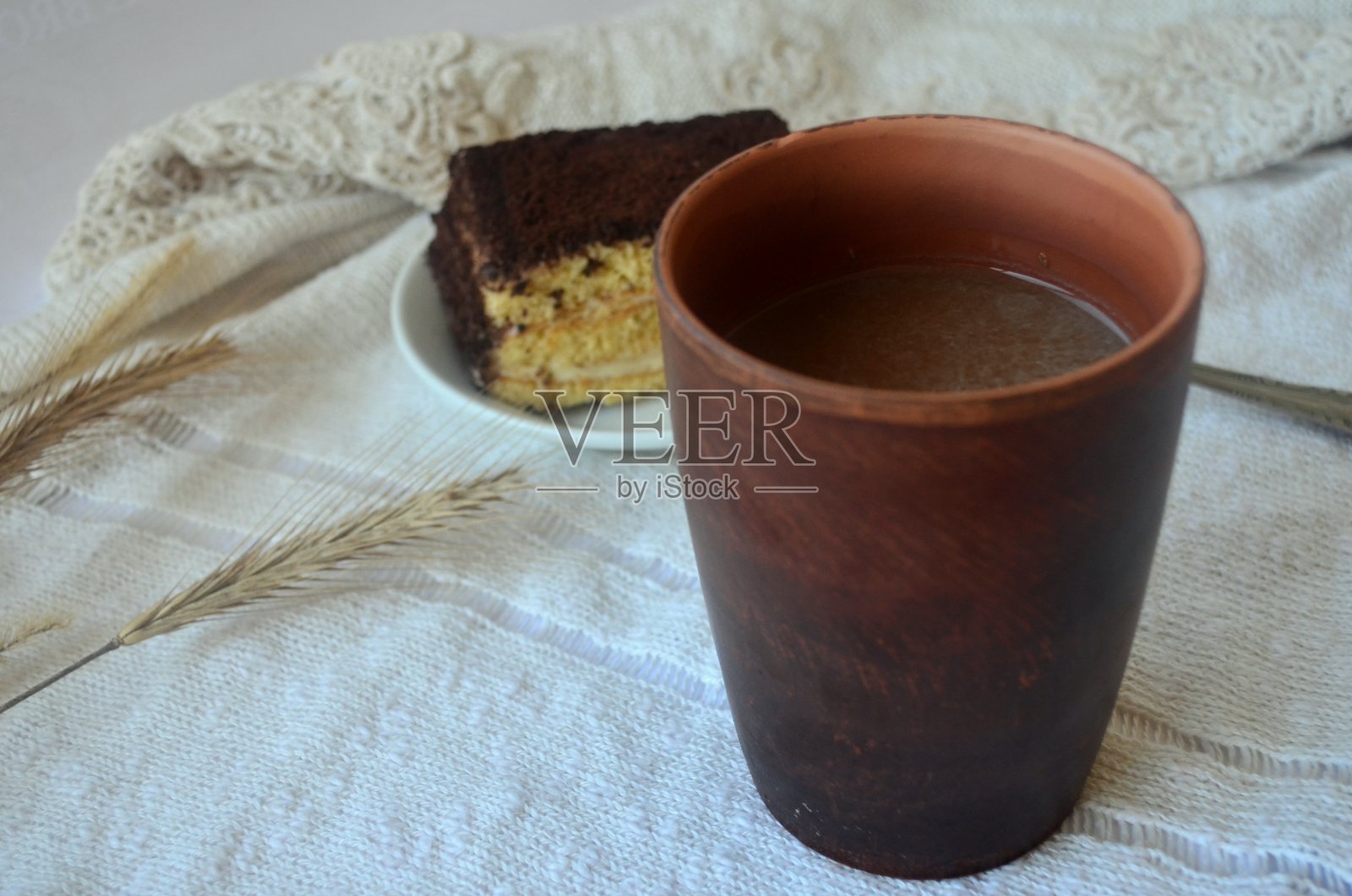 咖啡色陶瓷杯，蓬松的海绵蛋糕，白色盘子上放着银色勺子的提拉米苏，带花边的奶油色毛衣上放着干小麦穗。秋季布局的明信片。照片摄影图片