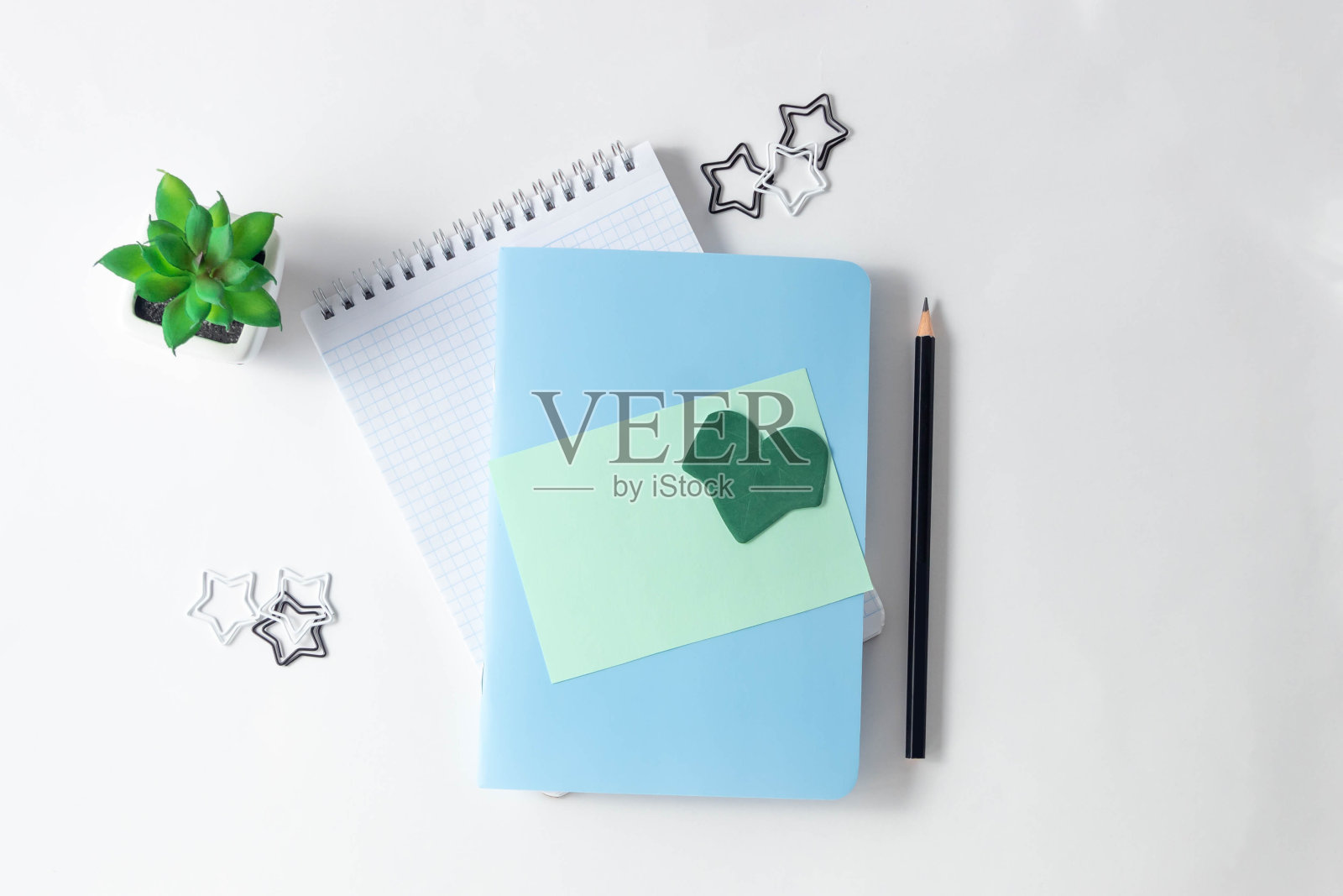 女性的工作场所。白色的桌子上放着记事本、空白的绿色纸和花。俯视图，平面布局，复制空间，极简主义。照片摄影图片