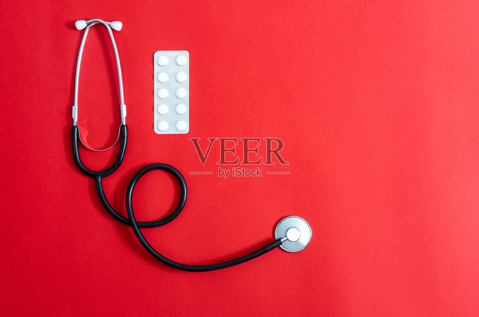 红色背景下放置听诊器和药丸照片摄影图片
