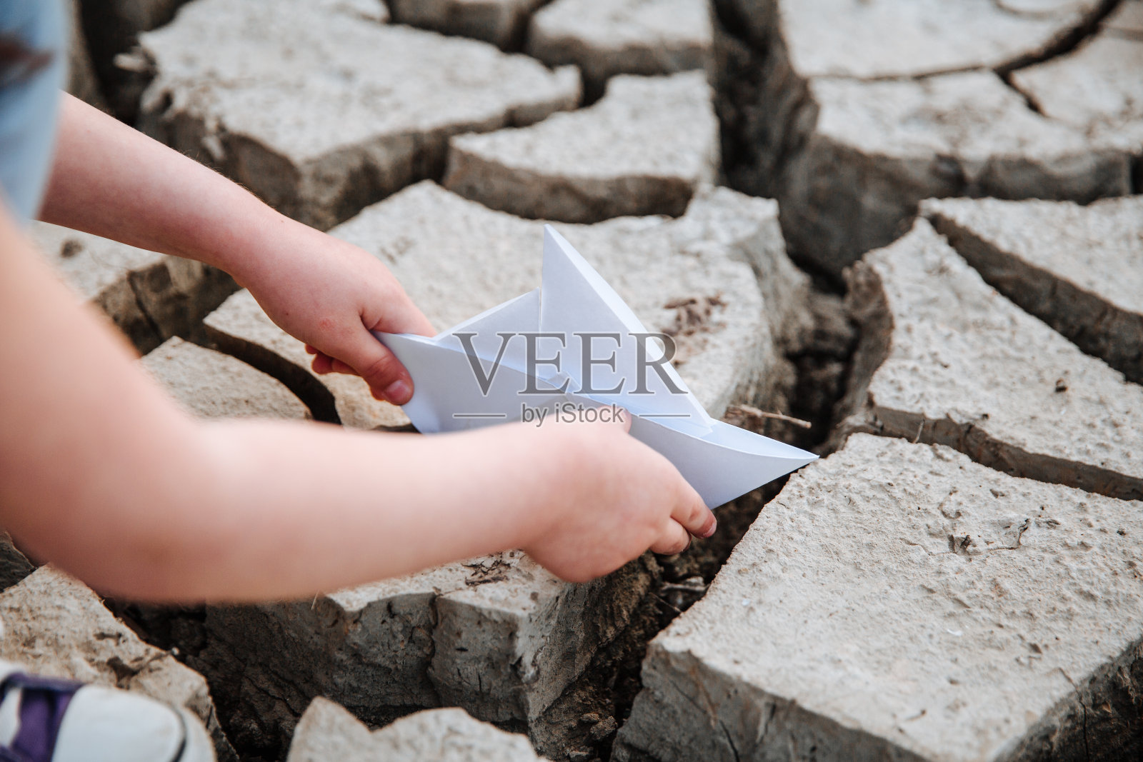 女孩把纸船放在干燥开裂的地面上照片摄影图片