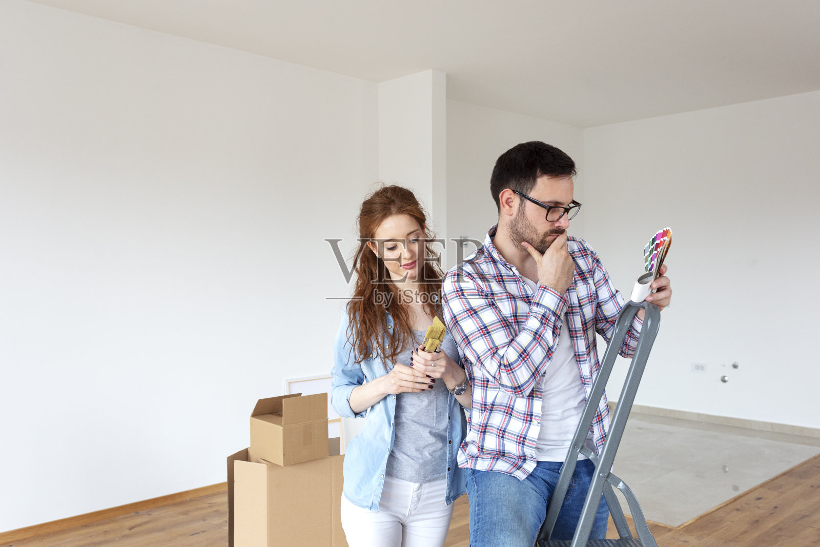 新房子里的夫妇计划如何刷墙，并观察颜色的样品与刷子在手照片摄影图片