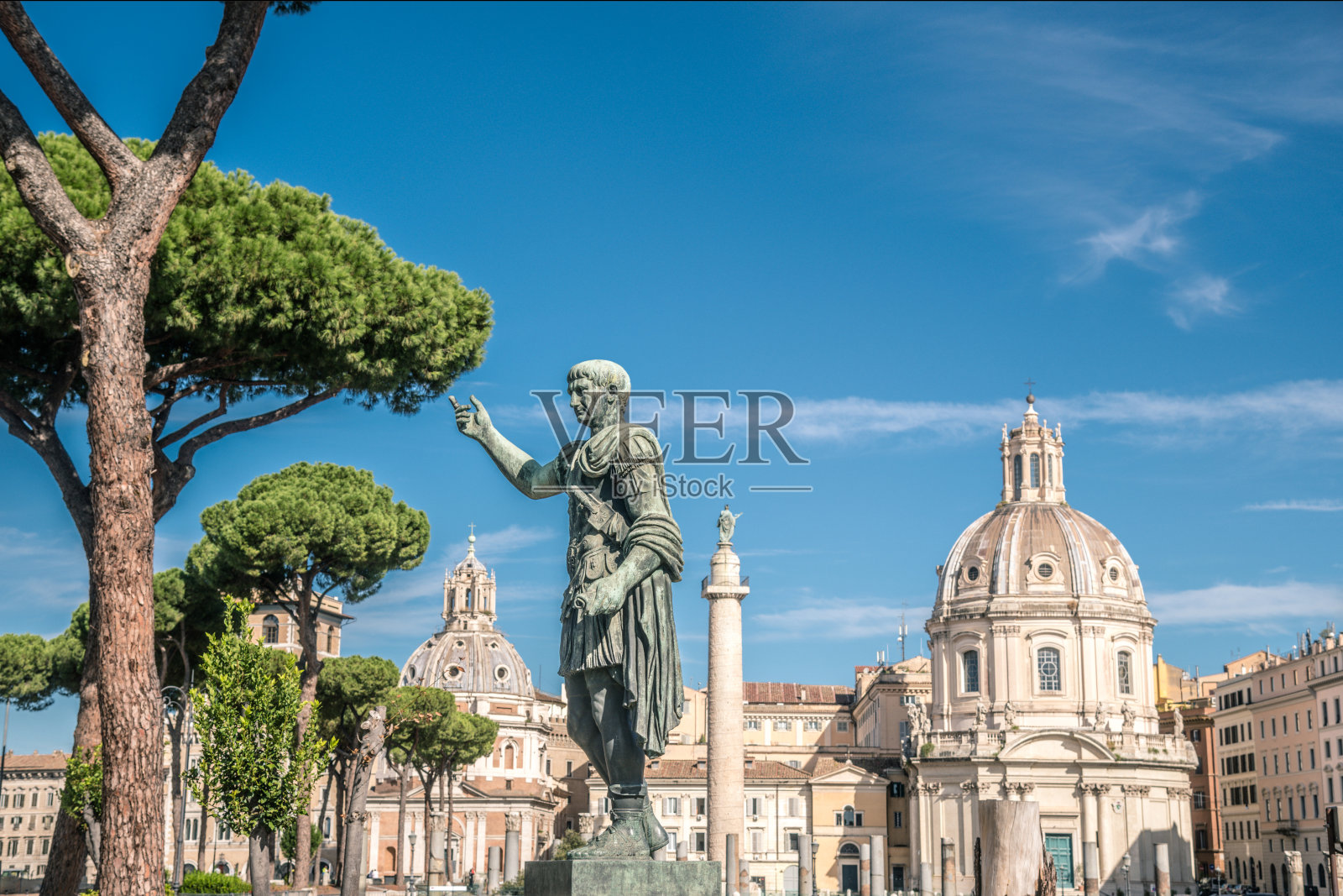 特拉亚诺的雕像与古代教堂和罗马城市的背景。一张来自意大利罗马的明信片，上面是一个晴朗的日子，天空湛蓝。美丽的天际线与历史建筑和罗马废墟照片摄影图片