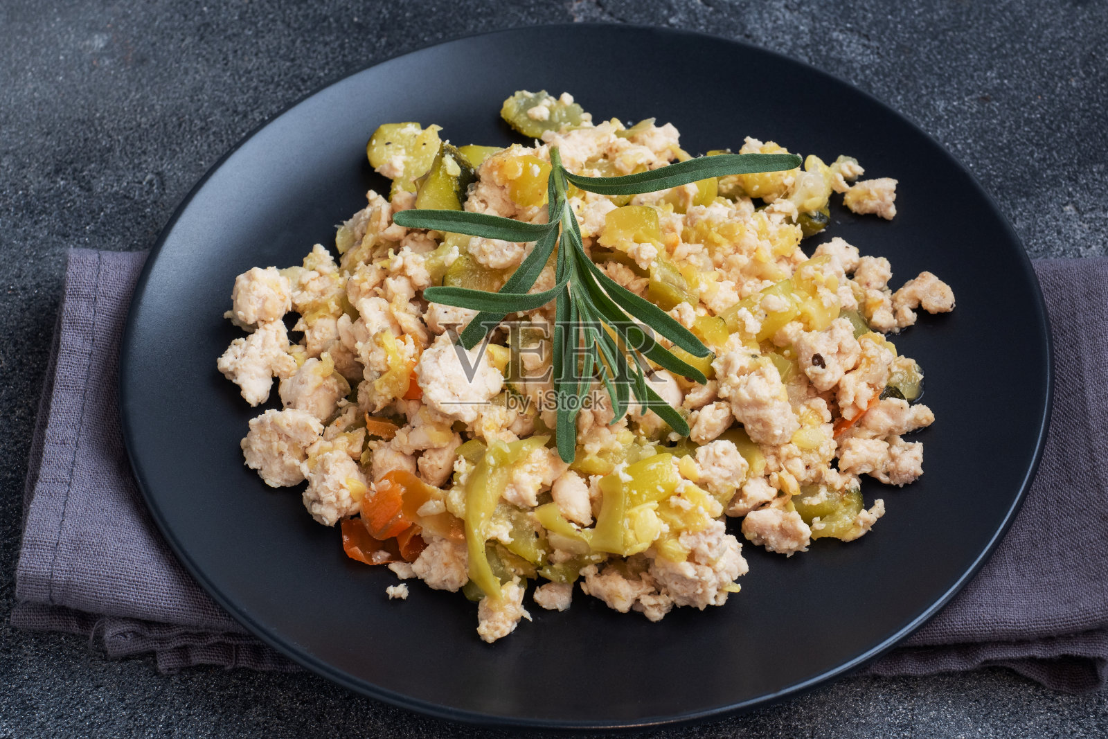 炖鸡肉末，蔬菜，西葫芦胡椒香料在一个黑色的盘子。照片摄影图片