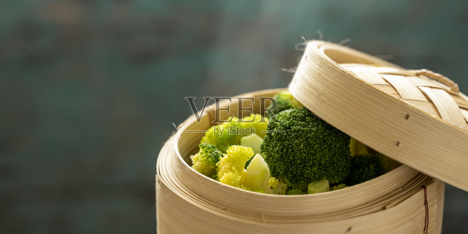 新鲜蒸花椰菜在竹制点心蒸笼上，抽象的蓝色/绿松石色风化木乡村桌子的背景。照片摄影图片