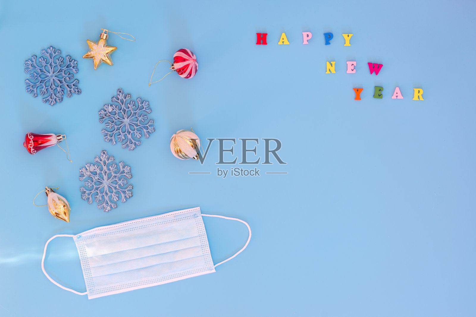 蓝色背景的圣诞玩具和医用面具。新年快乐。大流行期间的假日概念。明信片。本空间照片摄影图片