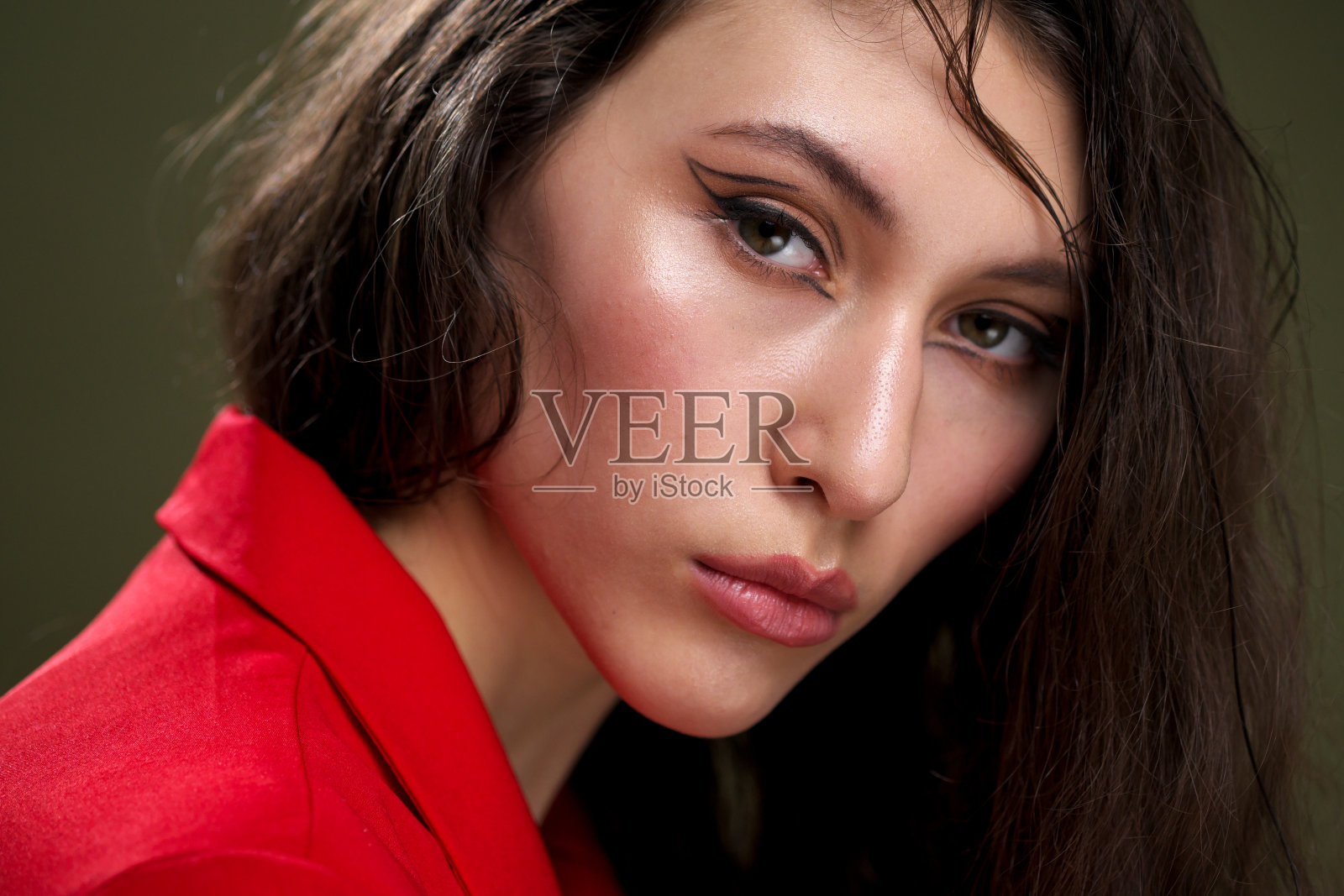 一个性感的年轻女子的肖像，穿着红色夹克，与潮湿的黑色长头发在工作室的绿色背景下摆姿势。照片摄影图片