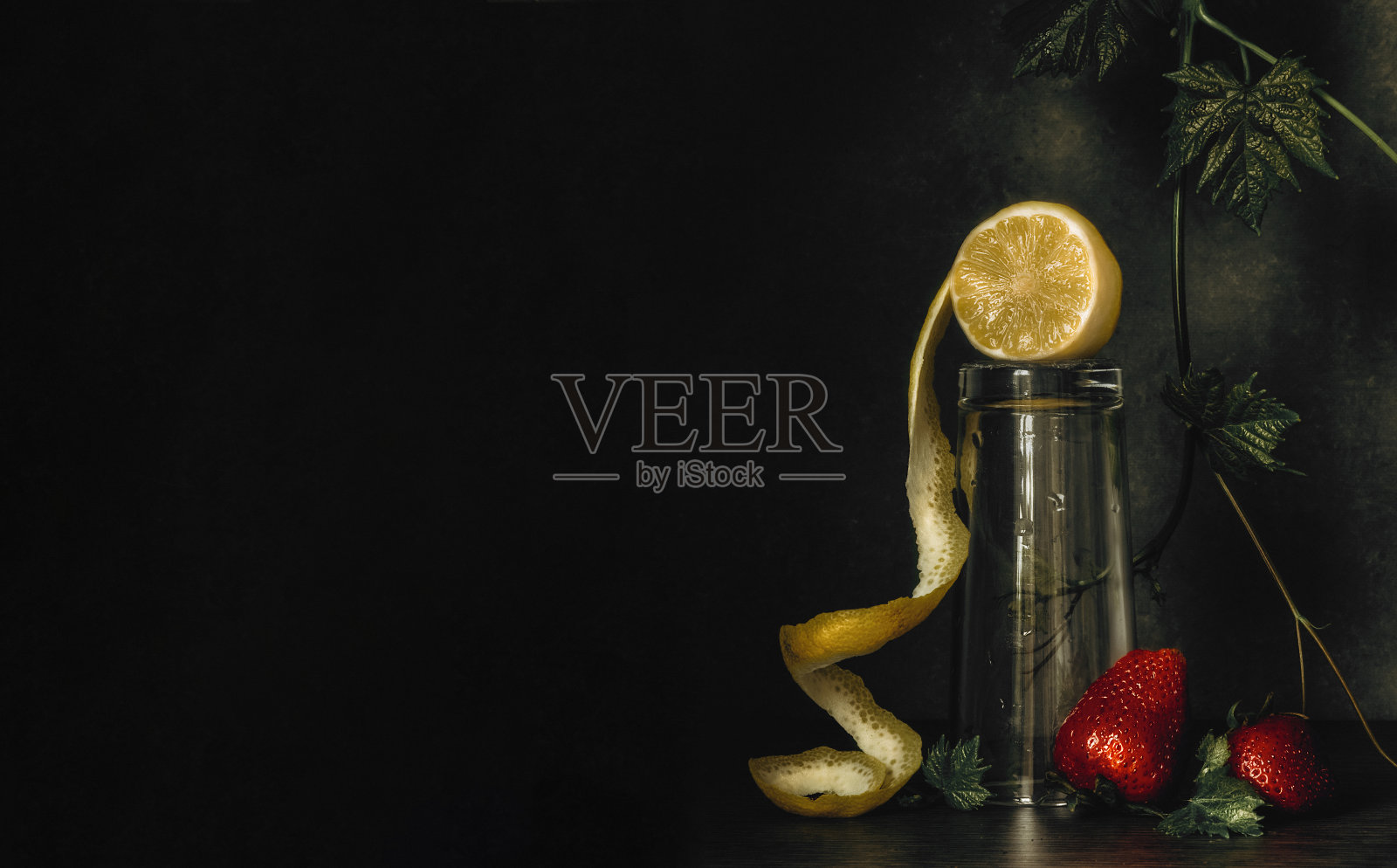 柠檬，葡萄叶和草莓的静态生活在一个黑暗的背景。照片摄影图片