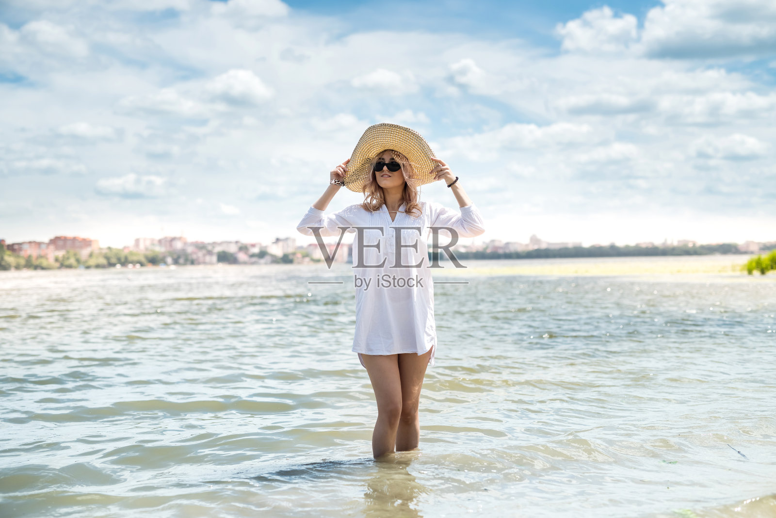 在一个炎热的夏日，穿着白色衬衫和草帽的女人在湖上散步照片摄影图片