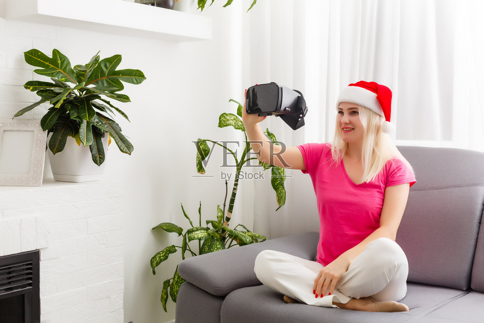 未来就是现在。迷人的年轻女子调整她的虚拟现实头盔和微笑而坐在家里照片摄影图片