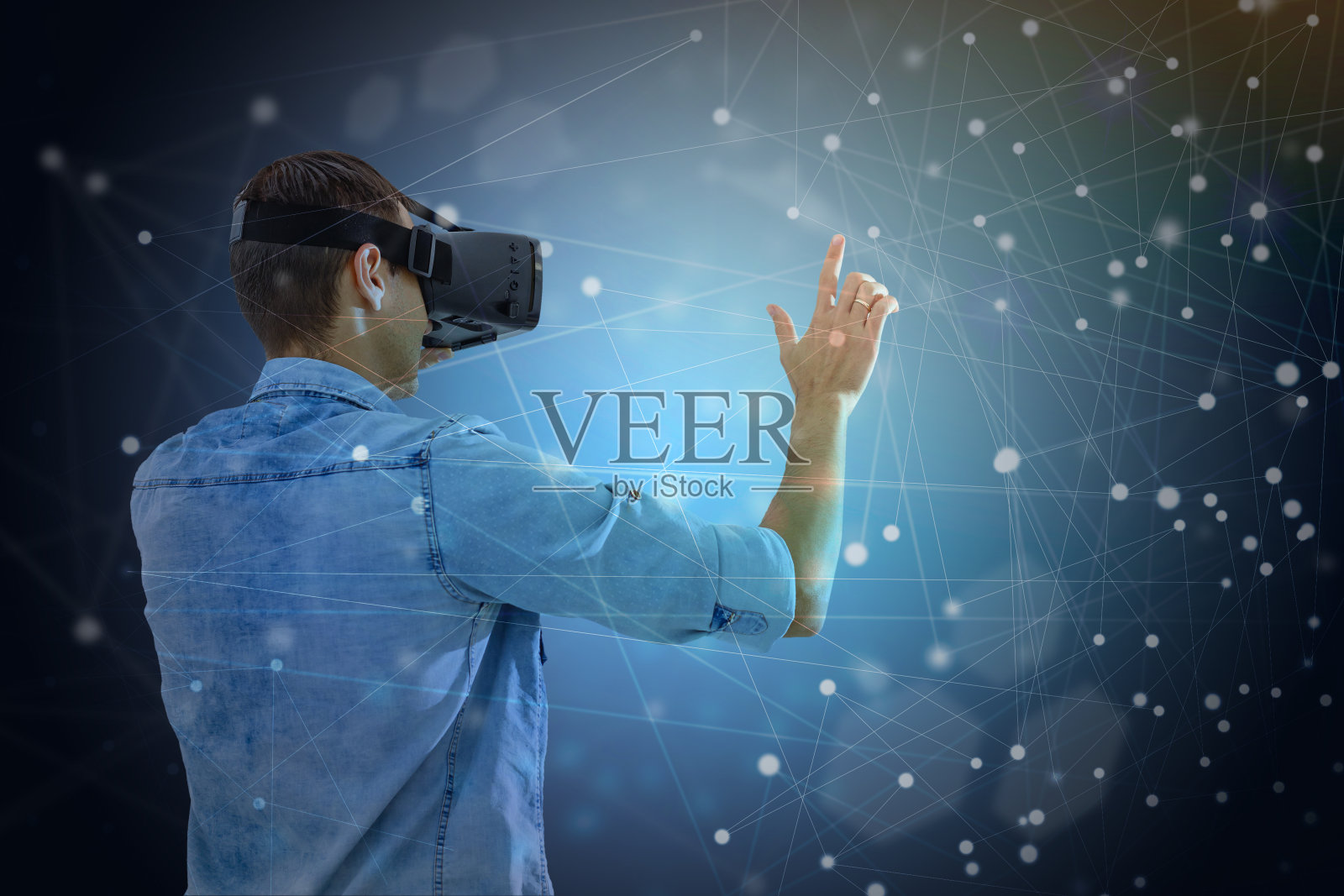 美丽的年轻人使用VR头盔，触摸空气在五颜六色的霓虹灯。戴着虚拟现实眼镜的人，在黑暗的魔法宇宙背景上，有蓝色的背光。照片摄影图片