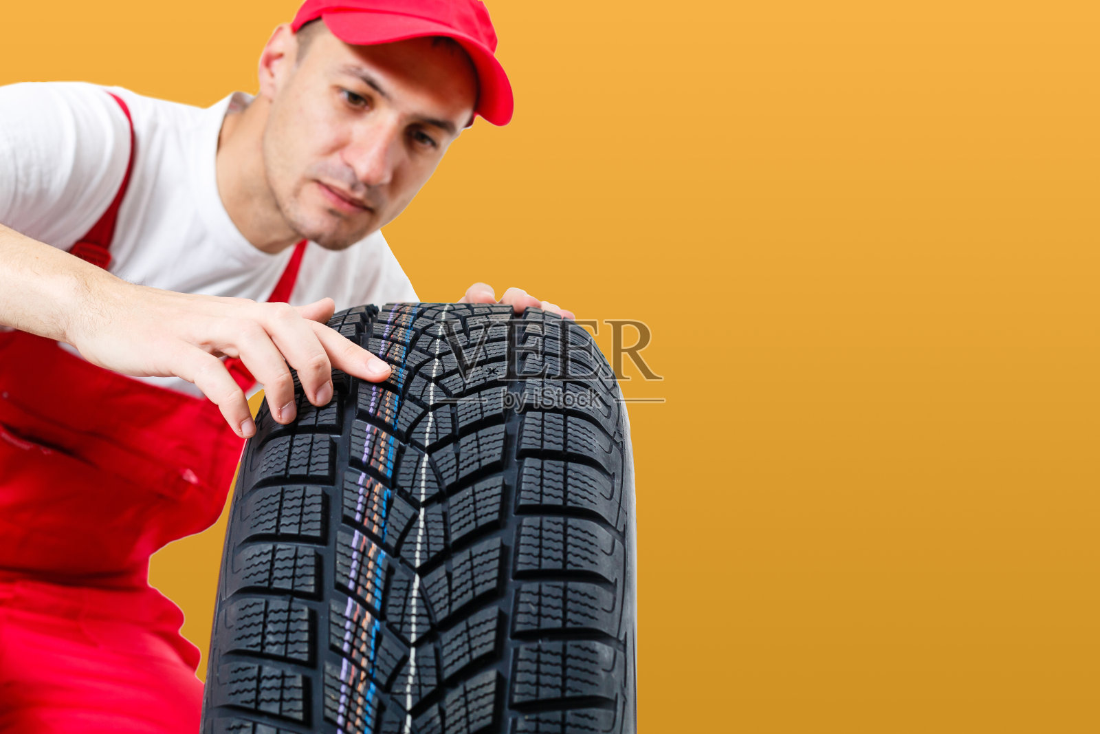 汽车技工携带轮胎在黄色的背景。快乐的人看着镜头微笑照片摄影图片