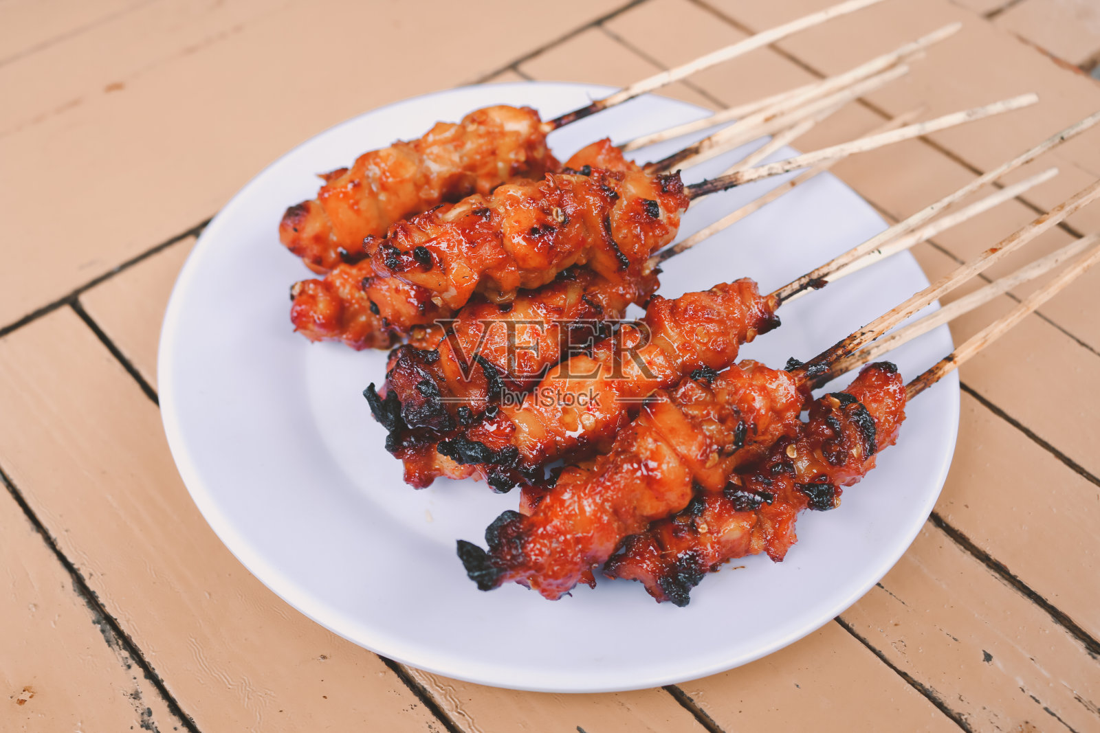 沙茶鸡肉或带有红色香料的沙茶鸡皮放在白色盘子里，单独放在木桌上照片摄影图片