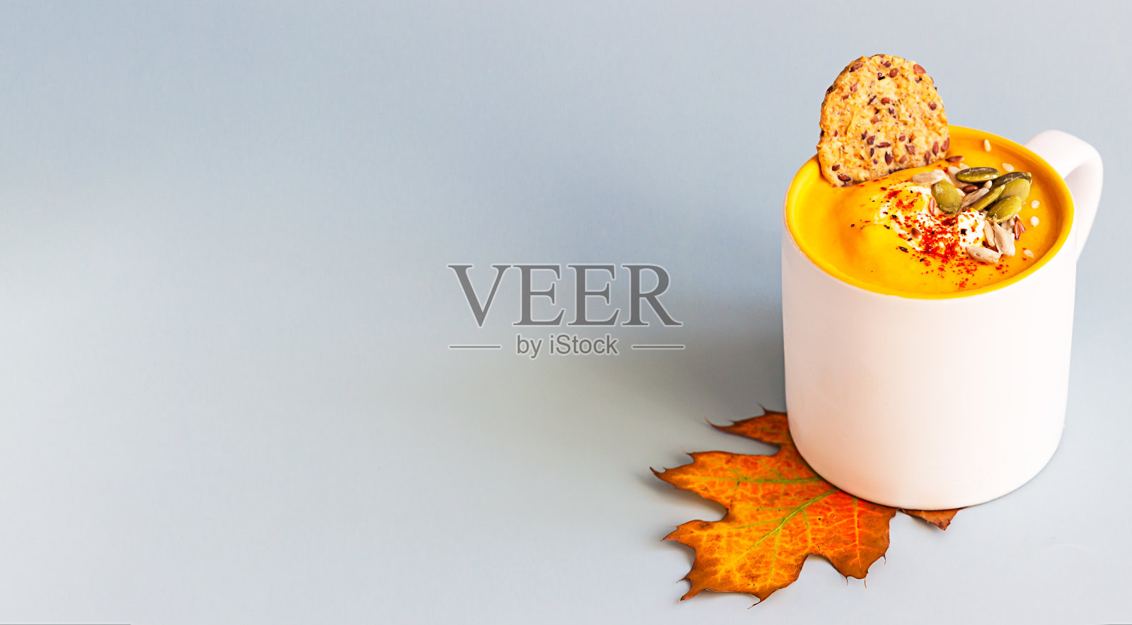 陶瓷杯南瓜奶油汤加种子和奶油，浅蓝色背景的杂粮健康饼干。照片摄影图片