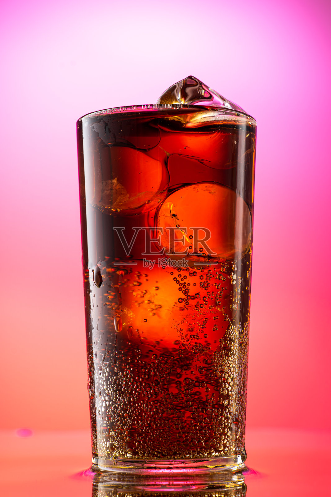 将可乐倒入一个有红紫色渐变背景的纯冰块的玻璃杯中照片摄影图片