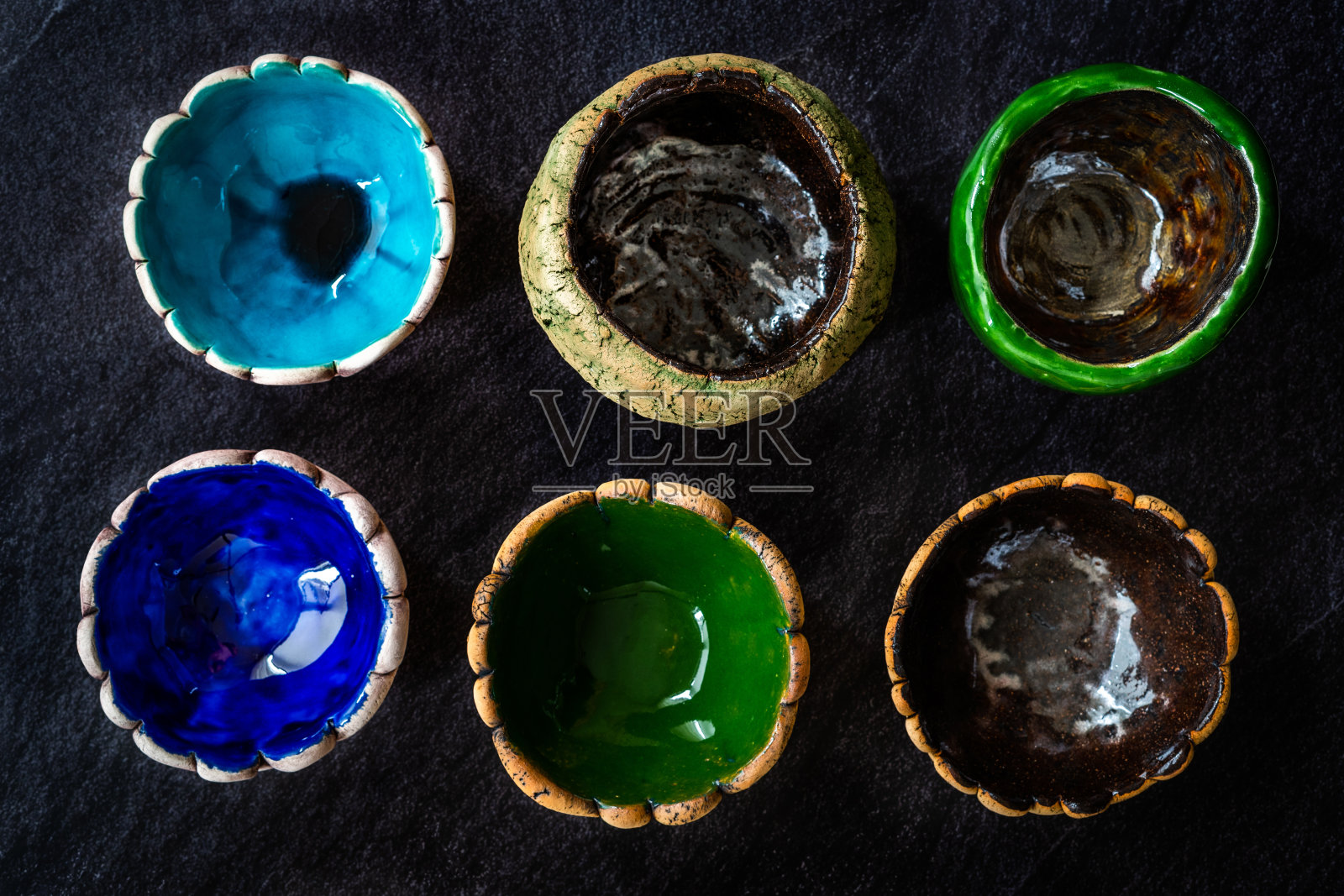 许多不同的明亮多彩的陶瓷碗和杯子手工制作/各种各样的深色表面和背景。照片摄影图片