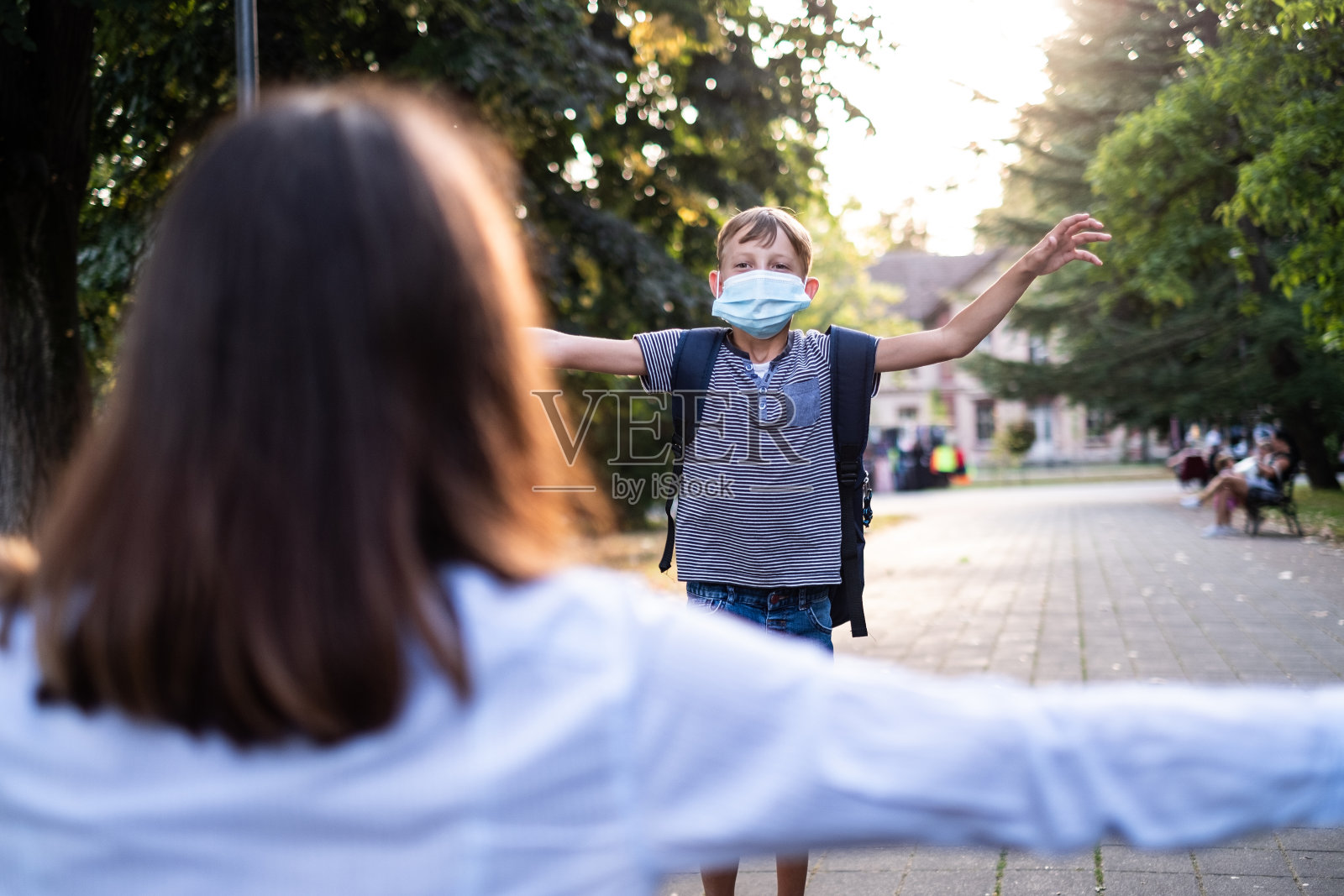 可爱的男孩从学校跑到妈妈的怀抱照片摄影图片