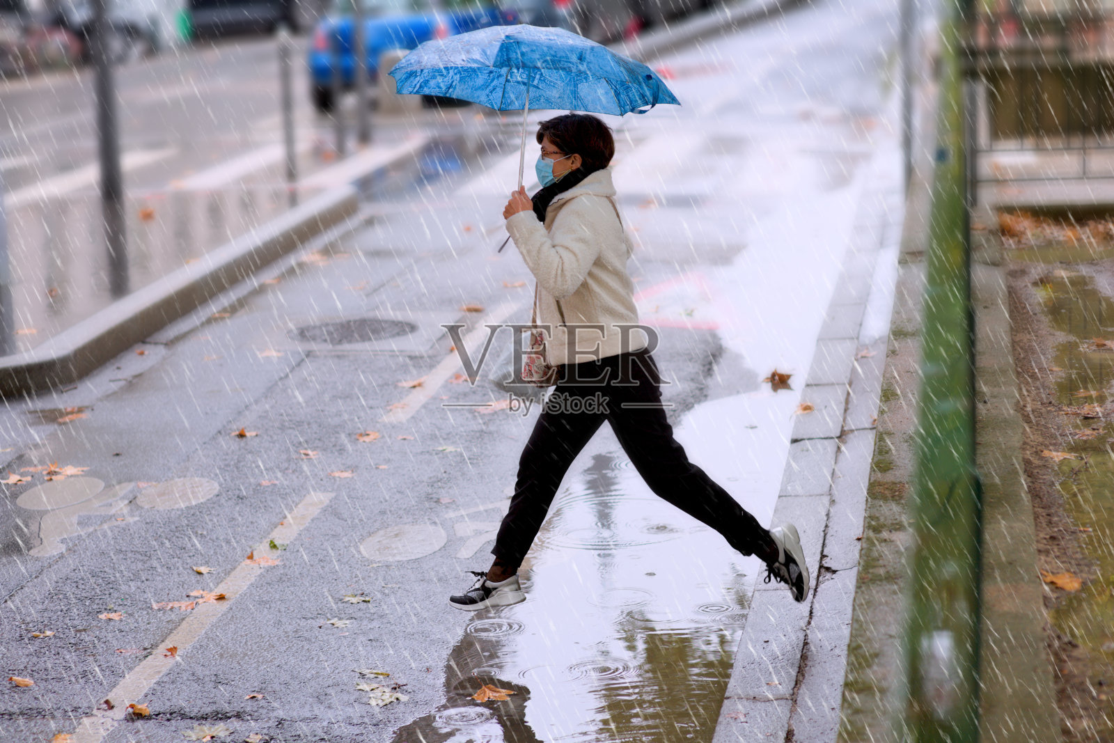 一个带着雨伞和防护面具的女人从水坑里跳了出来照片摄影图片