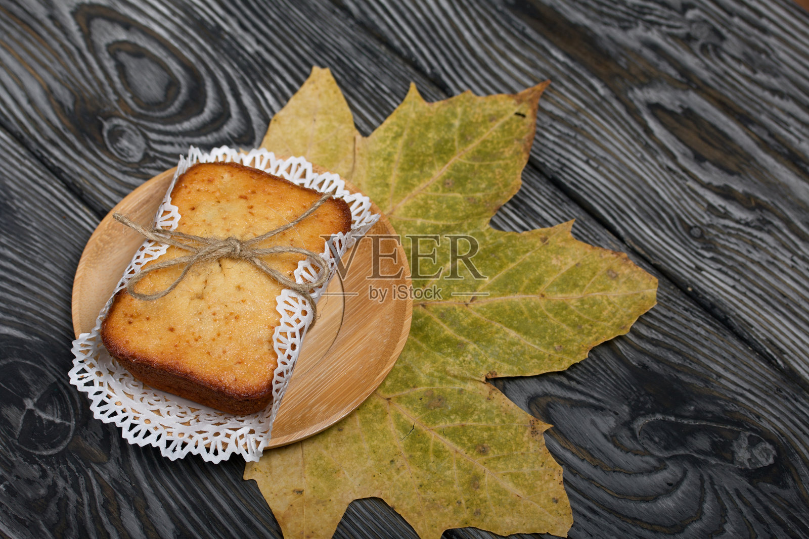 餐巾上刚烤好的纸杯蛋糕。与线。附近是一片干燥的枫叶。以黑色松木板为背景。照片摄影图片