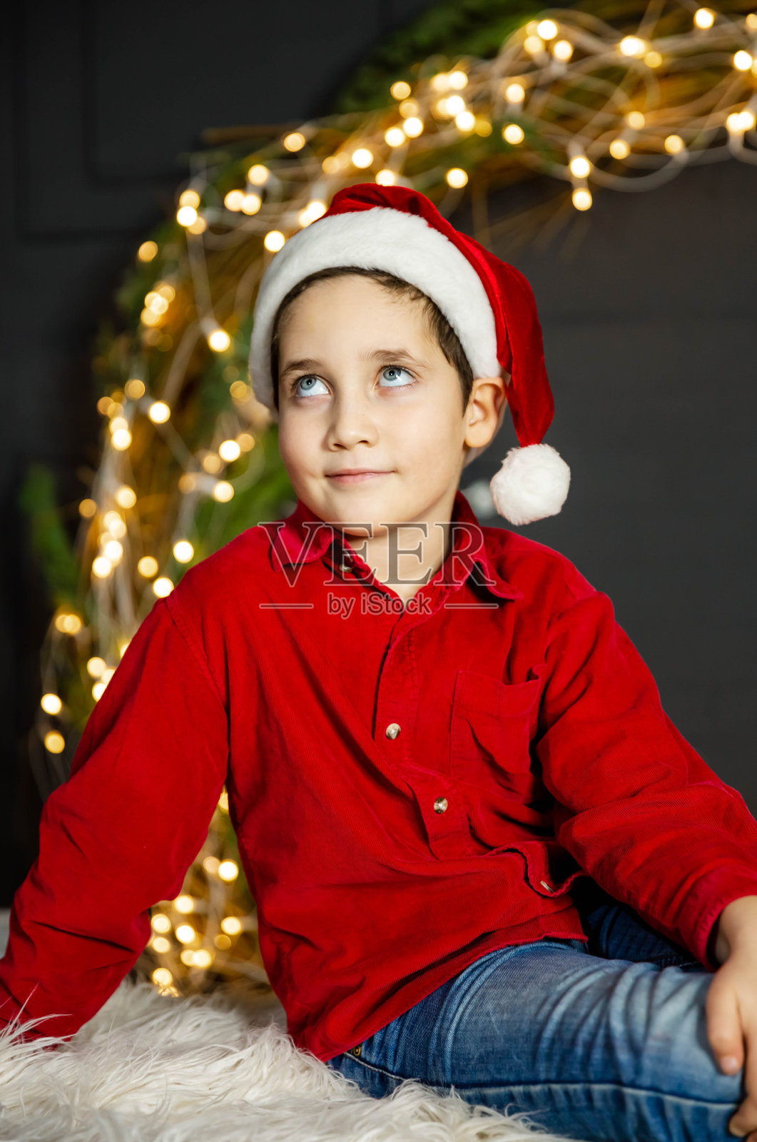 快乐的小男孩在家里玩。快乐的男孩戴着圣诞老人的红帽子照片摄影图片