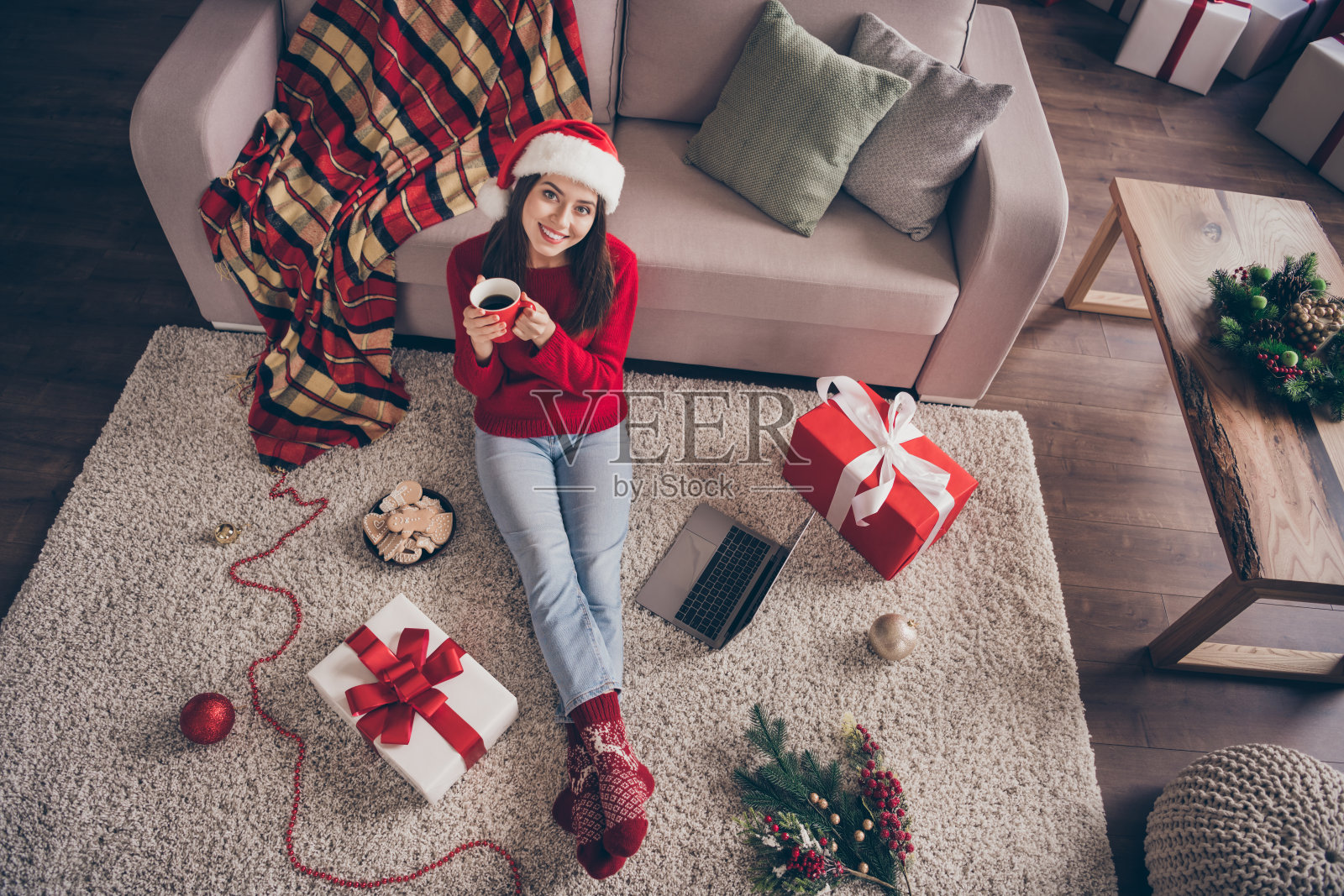 高的角度照片的女孩坐地毯上网本礼物，抱杯子，穿红色毛衣袜子牛仔裤在圣诞客厅室内照片摄影图片