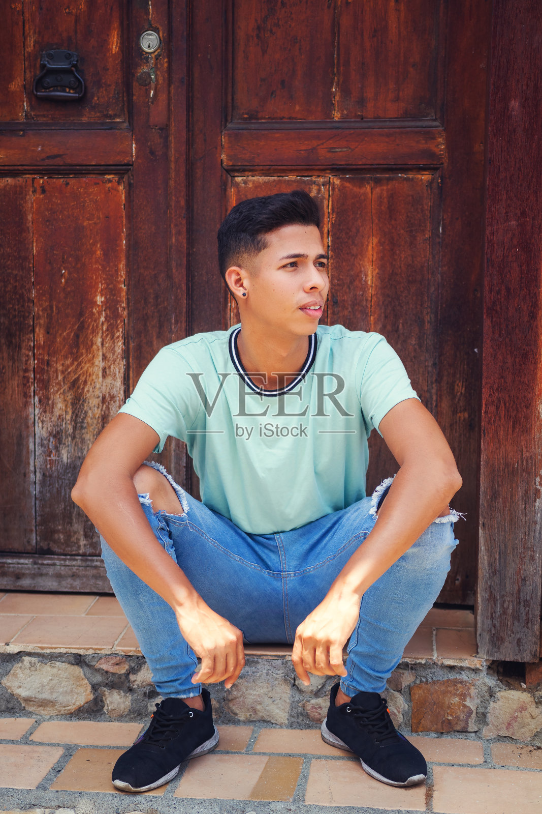 一个年轻人坐在一家老咖啡馆的墙门上照片摄影图片