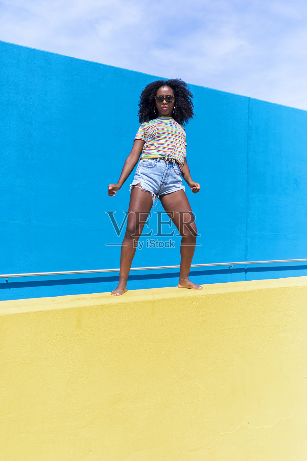 混血妇女肖像与大非洲卷发反对蓝色和黄色的墙跳舞，而看着相机照片摄影图片