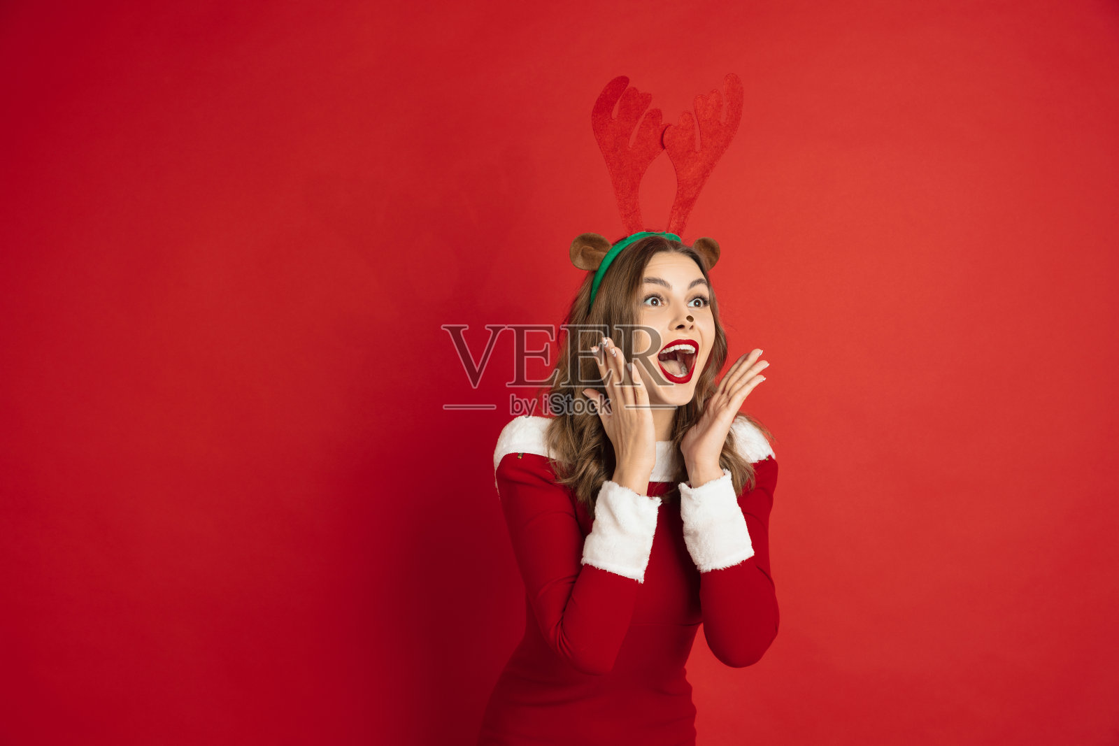 美丽的女人像圣诞鹿孤立在红色的背景。2021年新年的概念，冬天的心情，假期。照片摄影图片