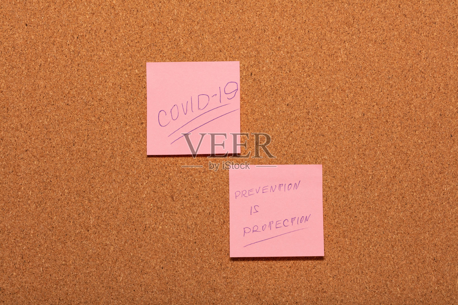 Covid-19和预防是在软木公告板上的两张粉红色贴纸上手写的“保护”。照片摄影图片