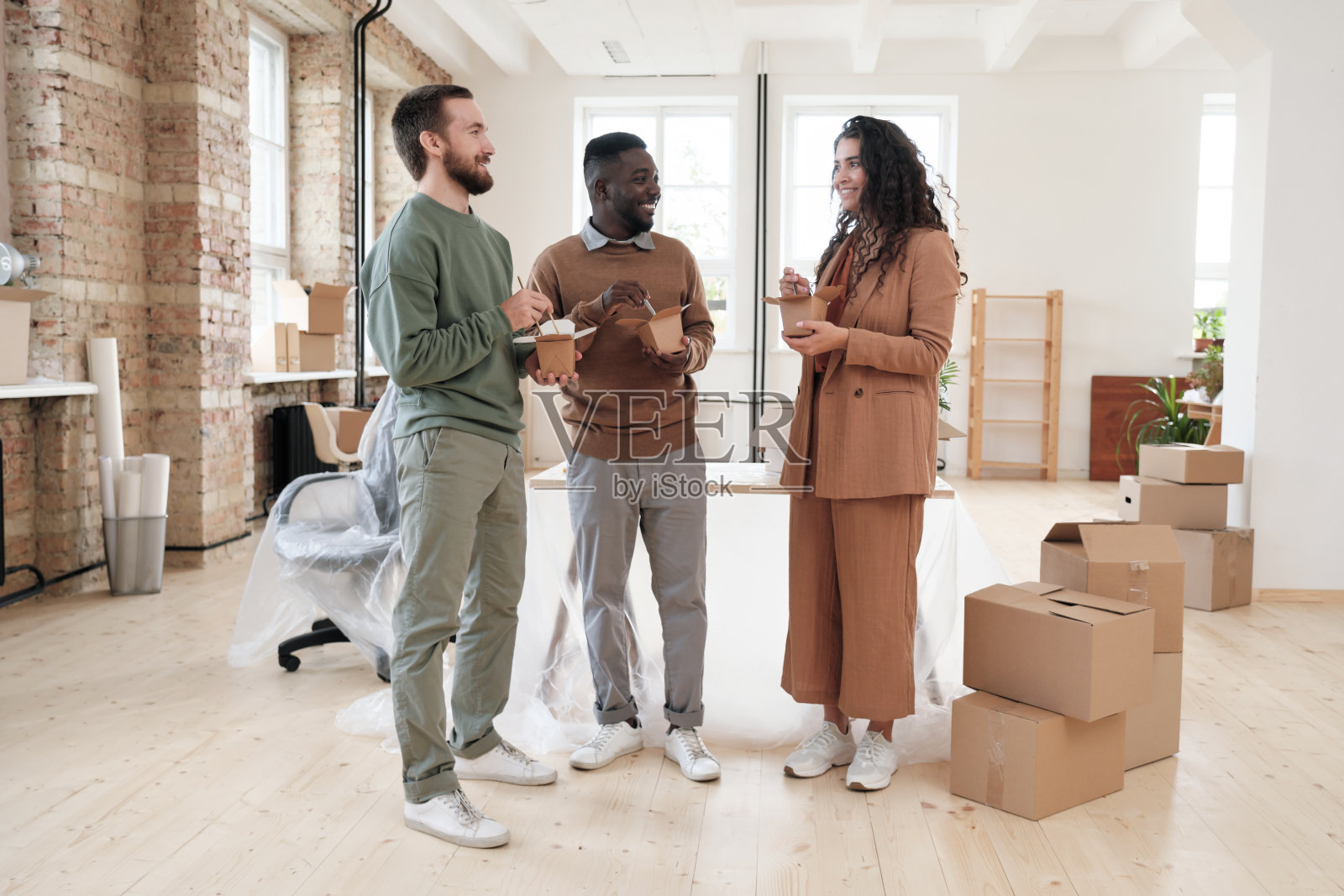 一群来自不同民族的年轻同事微笑着站在新办公室里，搬着箱子，一边吃着中餐一边交流照片摄影图片