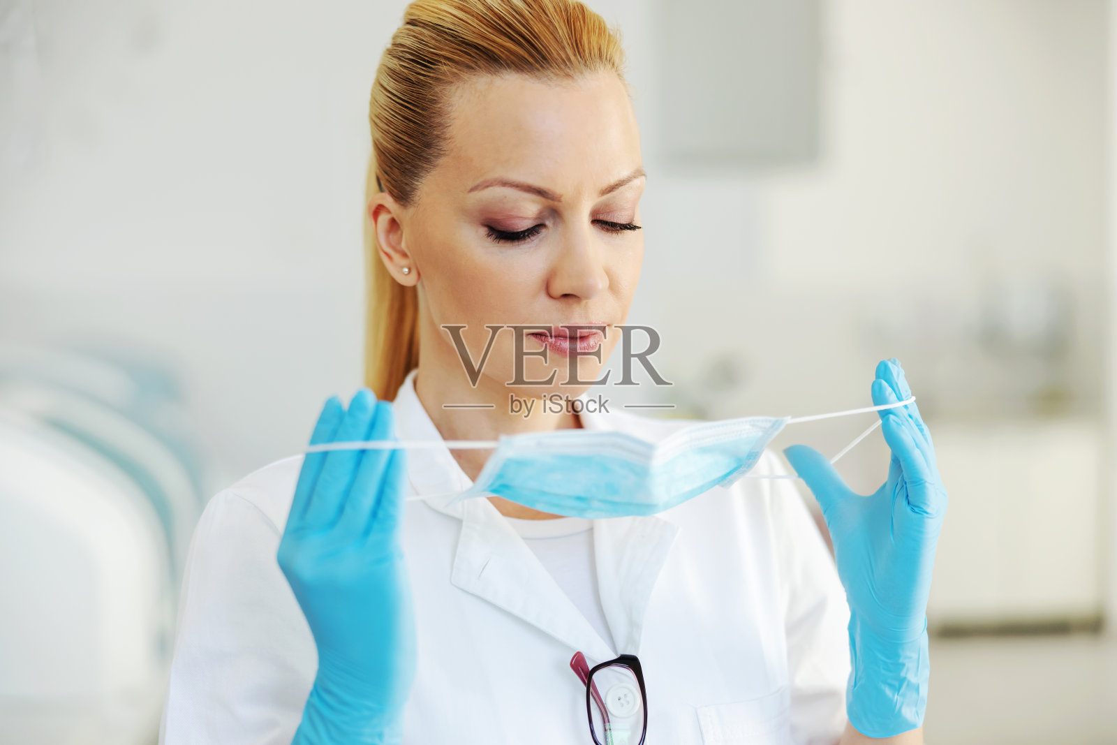 漂亮的金发实验室助理戴着橡胶手套站在医院里，戴着消毒口罩。照片摄影图片