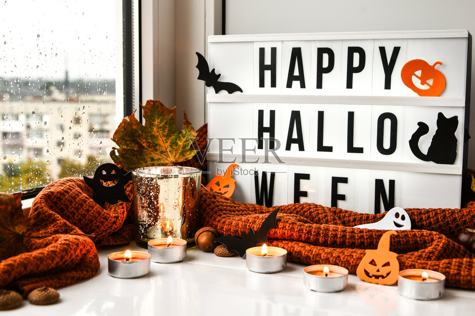 万圣节快乐。文字在白白的灯箱里，配上一件背景毛衣，晾干的树叶装饰在窗台上。多雨的窗口。鬼，南瓜蝙蝠，黑猫照片摄影图片