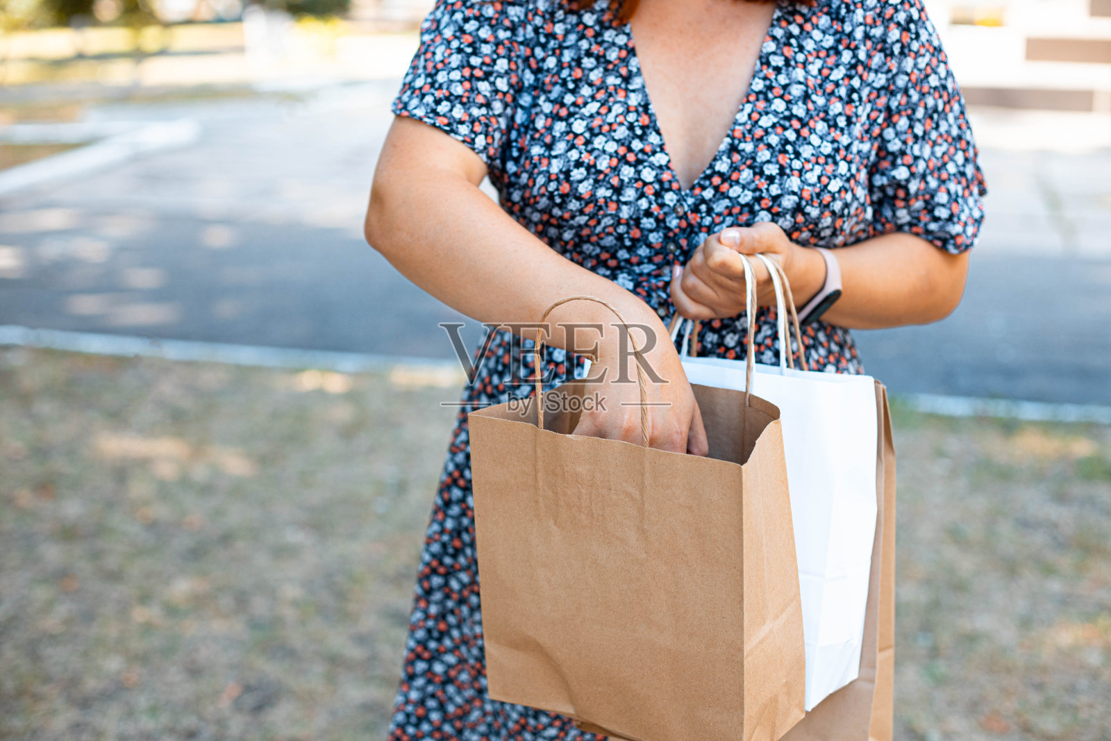在一个阳光明媚的日子里，一个女人在公园里拿着纸袋。送货服务的概念。照片摄影图片