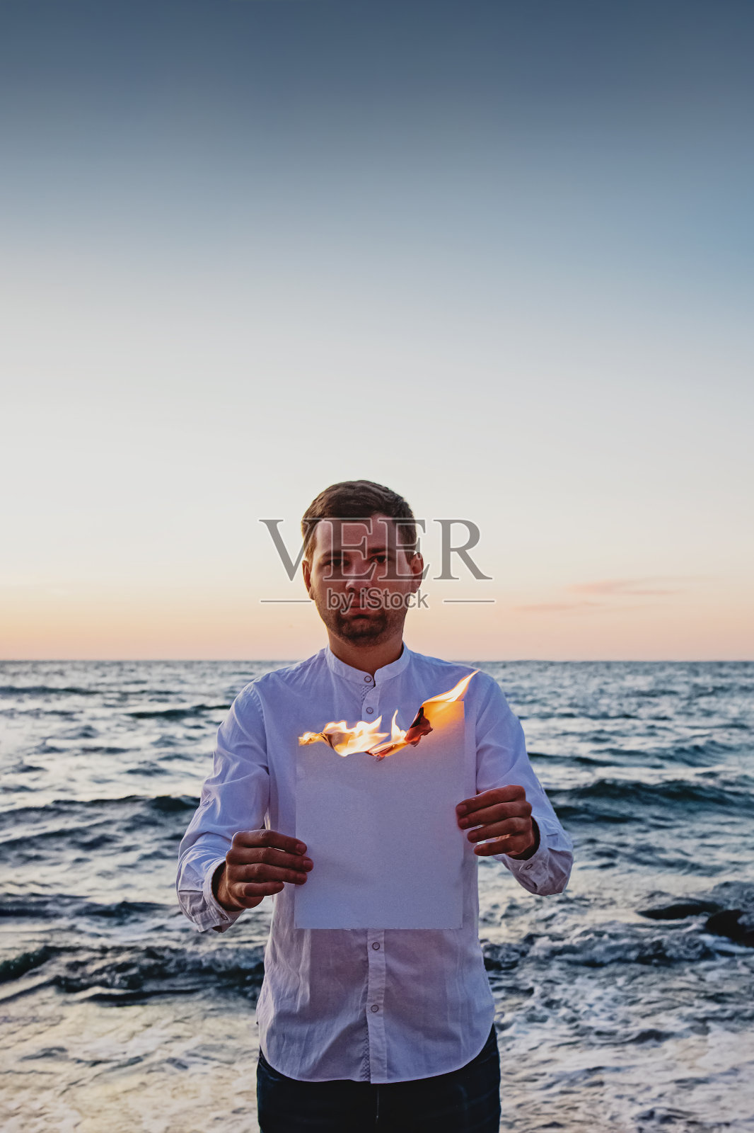 在大海的背景下，一个人拿着白色燃烧的纸。照片摄影图片