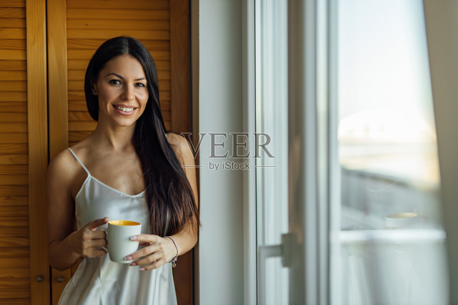 早晨的肖像，一个美丽的女人与一杯热饮，看着相机。照片摄影图片