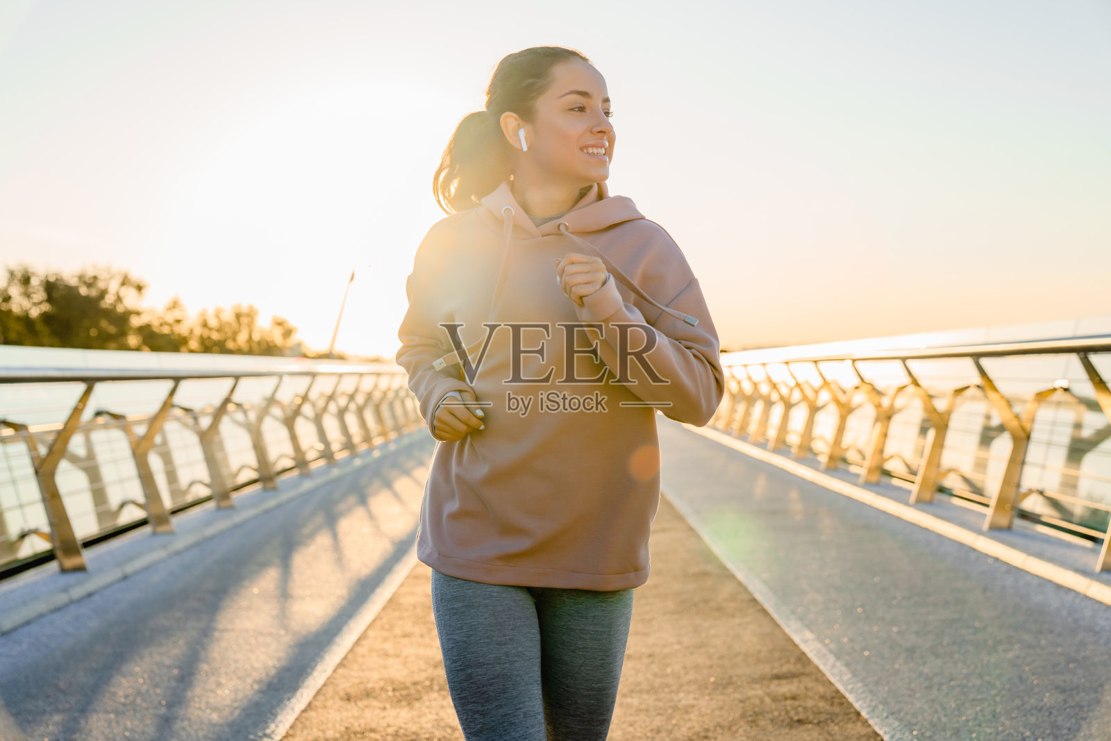 漂亮的年轻女子穿着运动服在桥上跑步。照片摄影图片