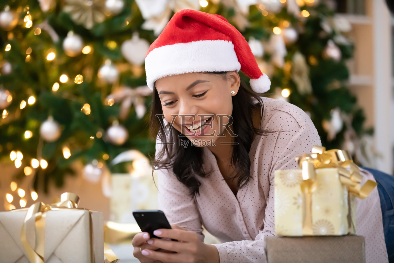 快乐的混血儿女人戴着圣诞帽用智能手机照片摄影图片