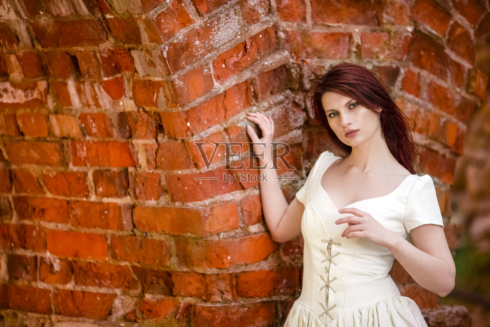 独特的古色古香砖墙映衬着松弛的红发女性画像。水平的形象照片摄影图片