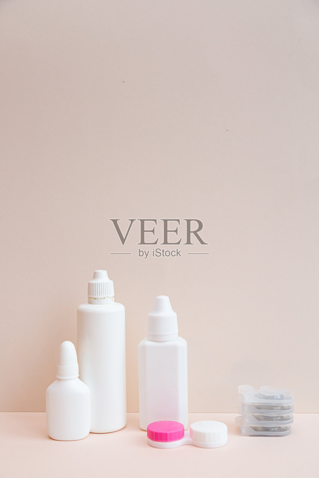 浅粉色背景上的隐形眼镜和隐形眼镜护理产品照片摄影图片