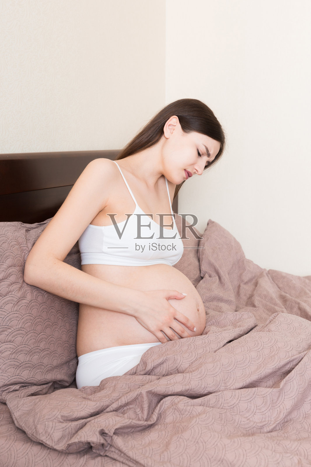 年轻漂亮的孕妇，在痛苦中，坐在卧室的床上，准备分娩照片摄影图片