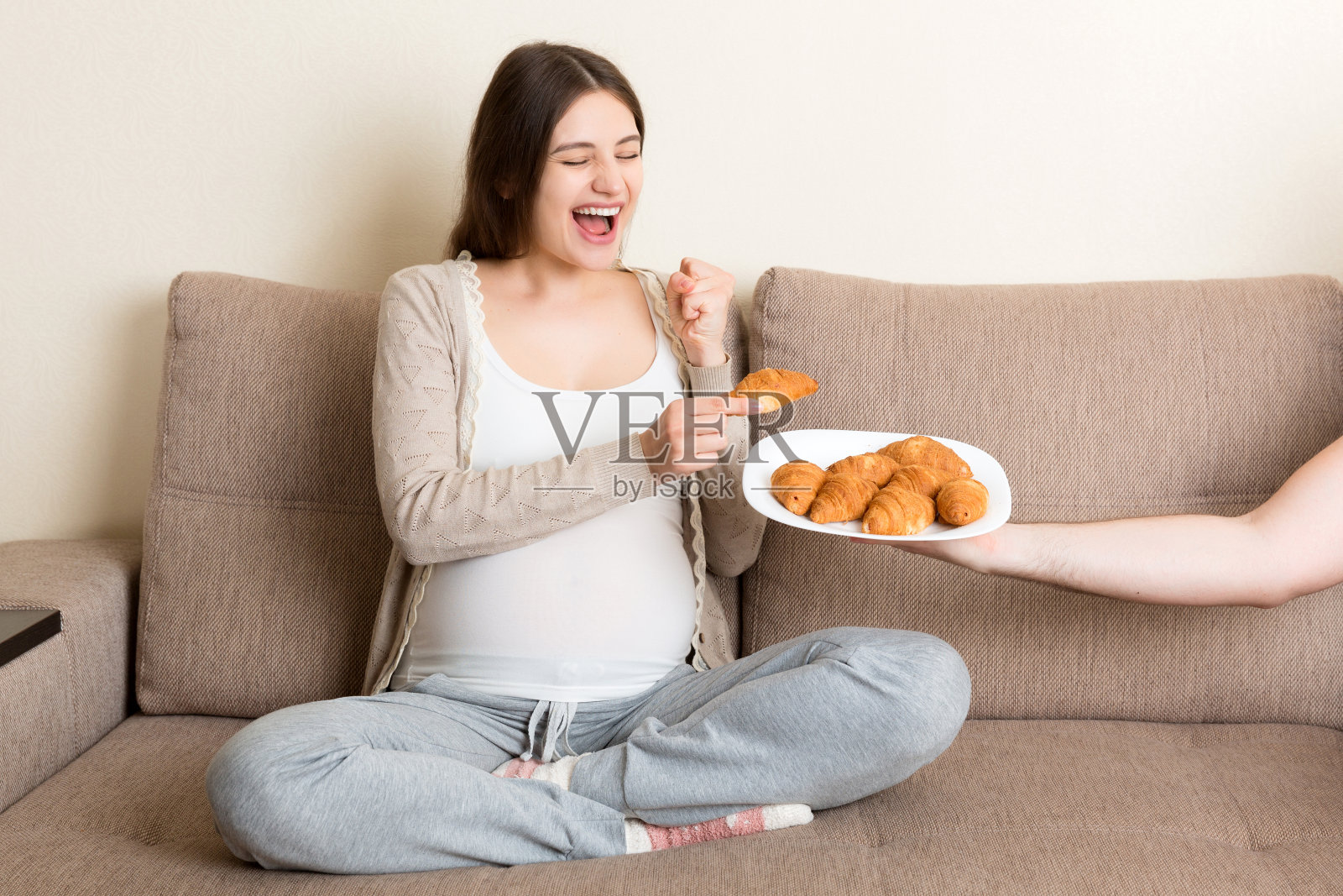 丈夫为怀孕的妻子提供牛角面包，在沙发上放松，准爸爸照顾准妈妈照片摄影图片