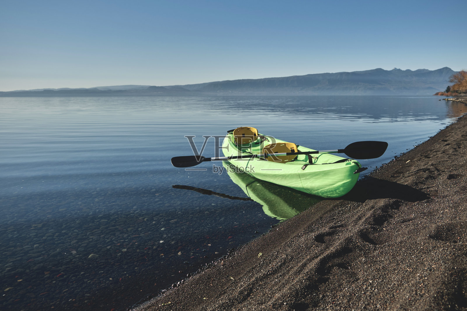 沙滩边一艘没有人划桨的空绿色皮划艇。照片摄影图片