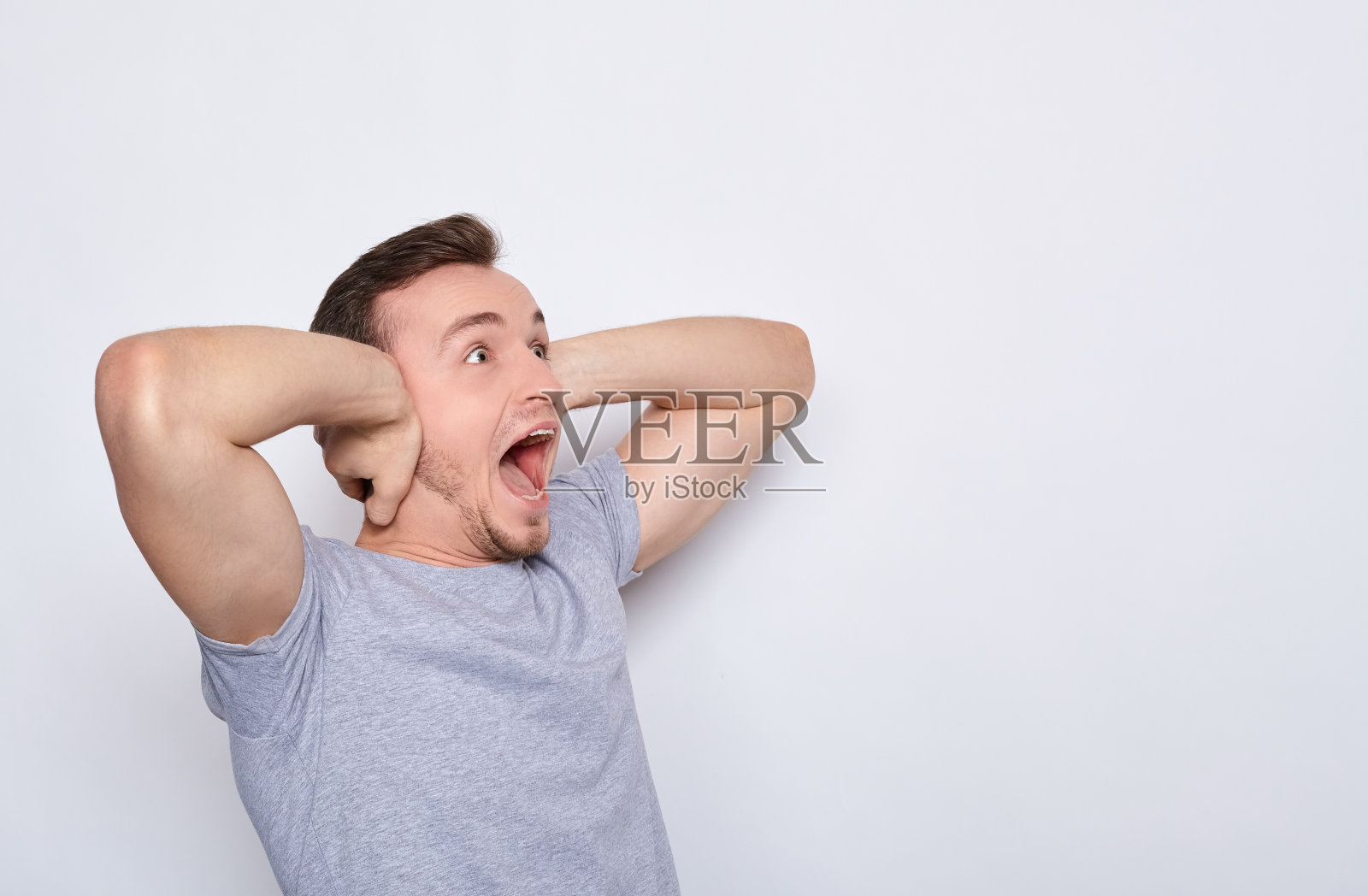 愤怒、震惊的年轻人尖叫起来，并用手捂住了耳朵。照片摄影图片