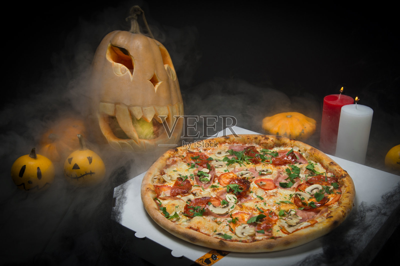 万圣节装饰中的肉披萨:画着脸的可怕的南瓜，燃烧着的蜡烛上冒着恐怖的烟雾照片摄影图片