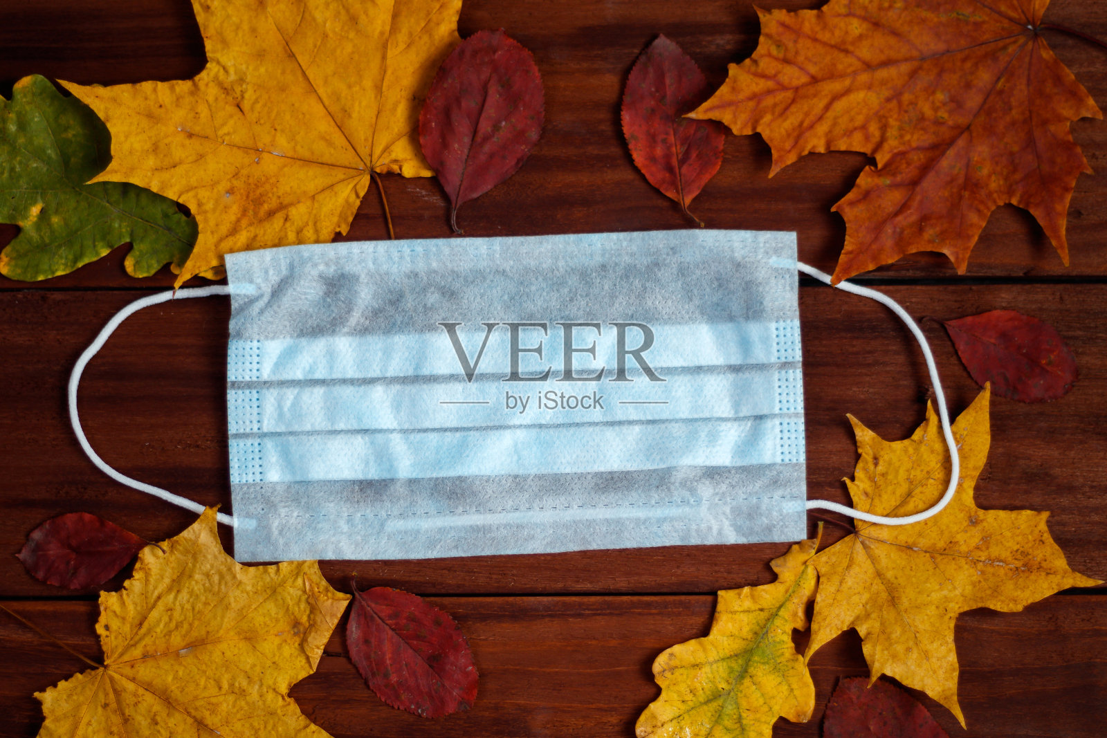 手术口罩的背景秋天的树叶。冠状病毒的概念。照片摄影图片