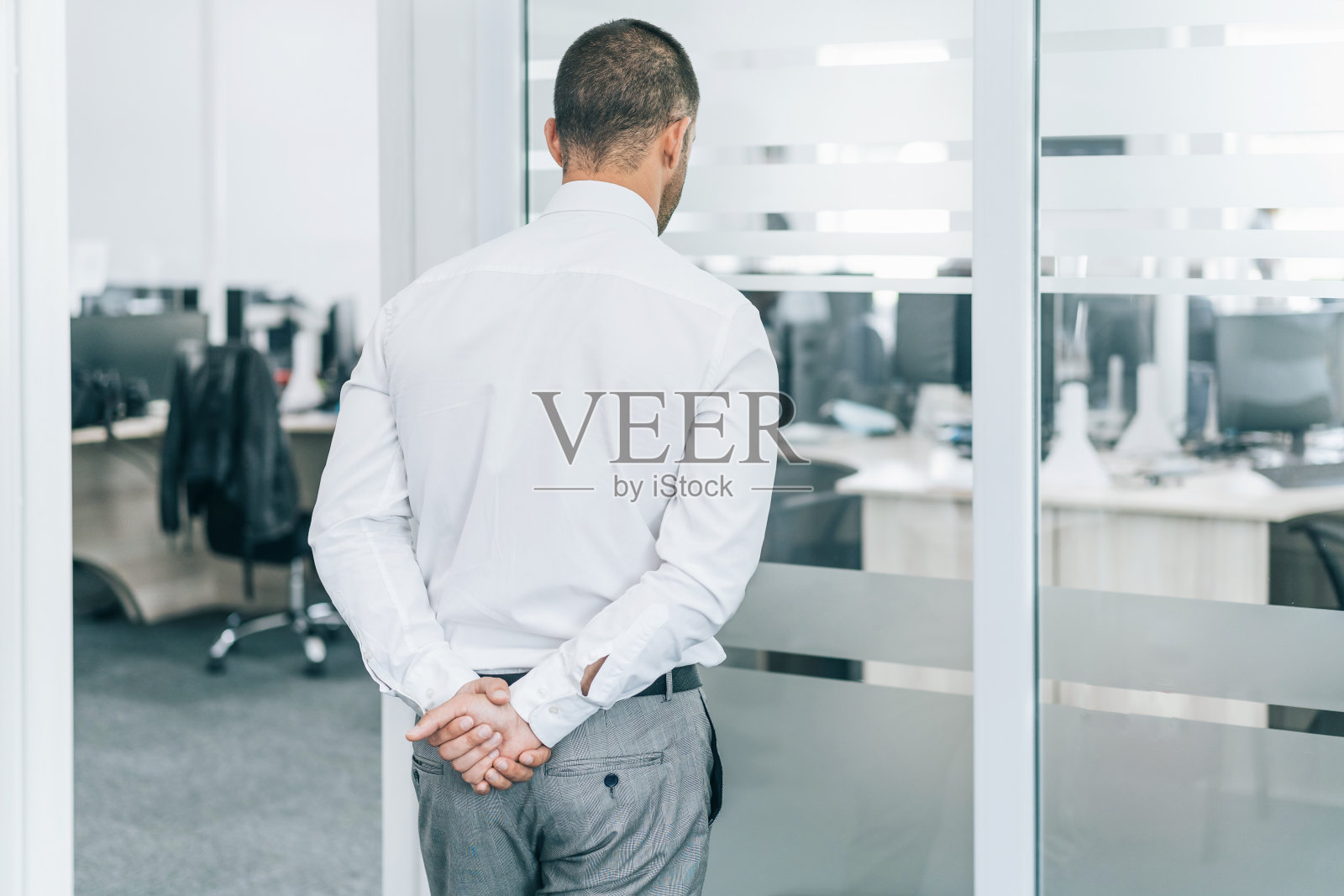 疫情期间，焦虑的商人双手背后，望着空荡荡的办公室照片摄影图片