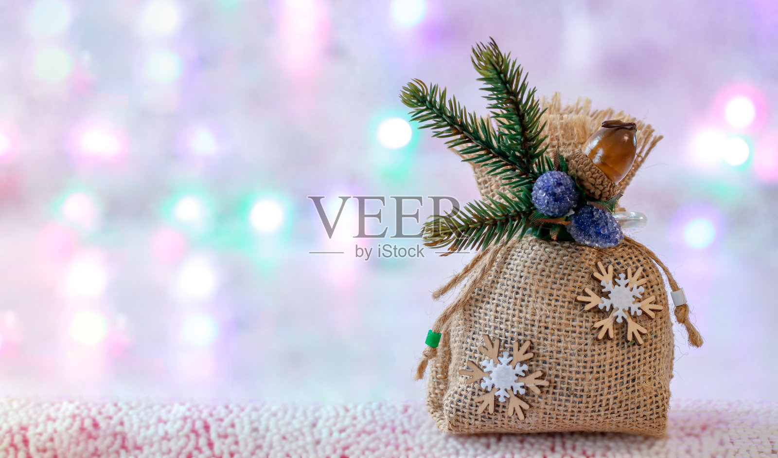 用粗麻布制成的圣诞礼物袋，装饰有雪花和冷杉枝在一个不集中的背景与灯的花环。节日,圣诞节的背景。复制的空闲空间。照片摄影图片