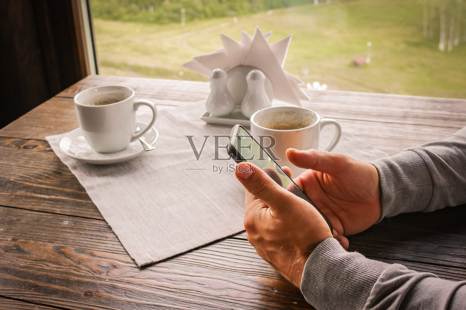 男人的手拿着智能手机。阅读新闻，在咖啡馆的桌子上用一杯咖啡或茶拨打消息。照片摄影图片