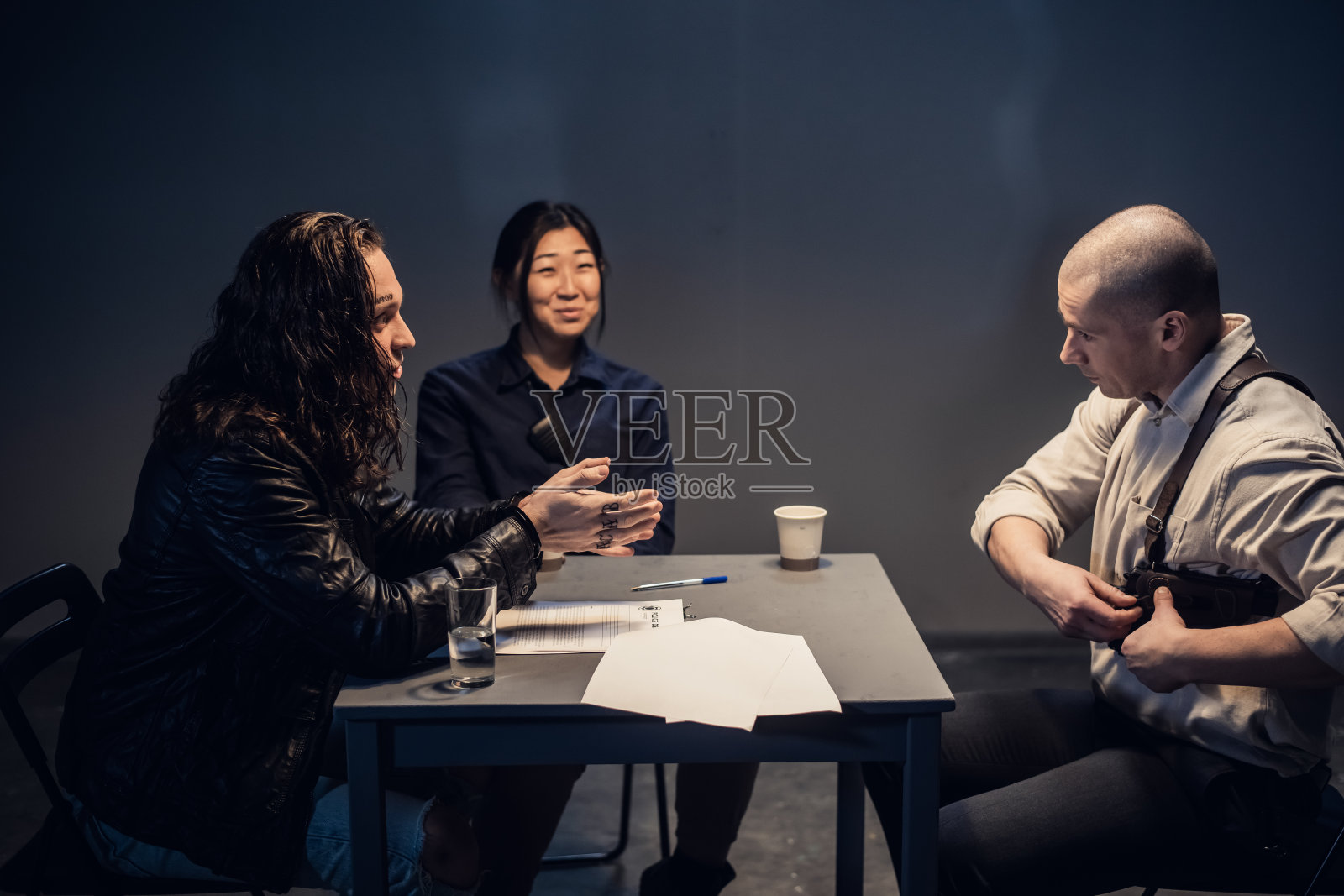 两名警察正在审问一名有面部纹身和长发的男子，此人涉嫌犯罪。考虑一下本案中的证据照片摄影图片
