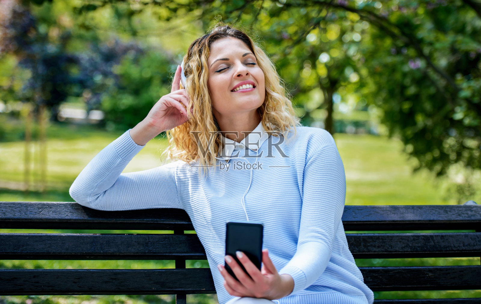 年轻女子在公园里用智能手机和耳机听音乐。生活方式、技术概念照片摄影图片